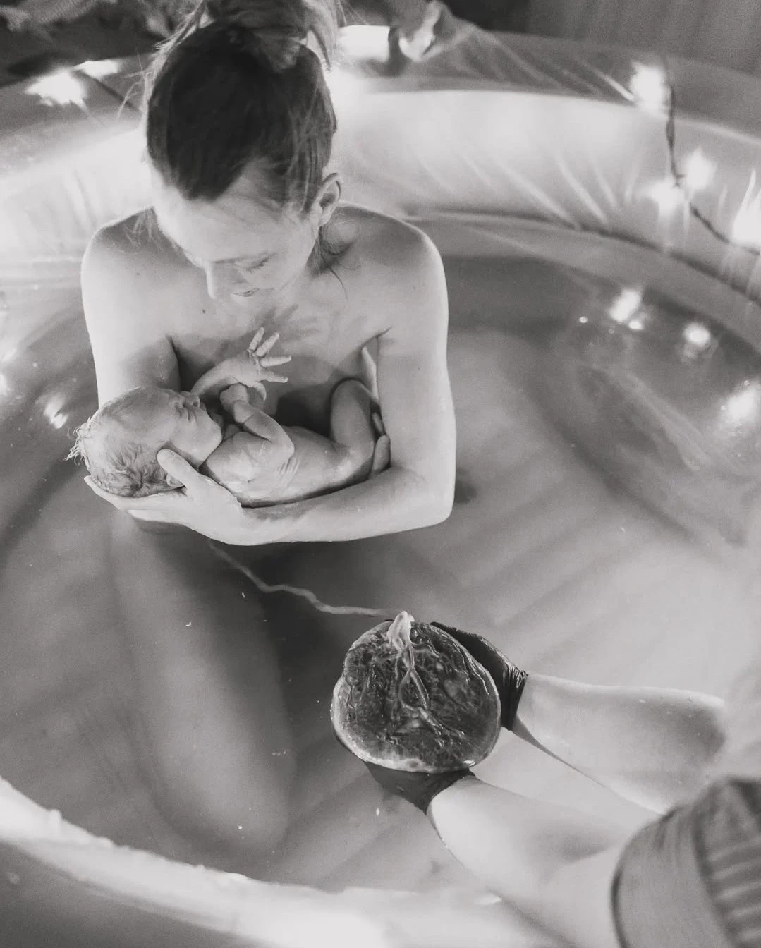 En mamma håller sitt nyfödda barn i en birth pool
